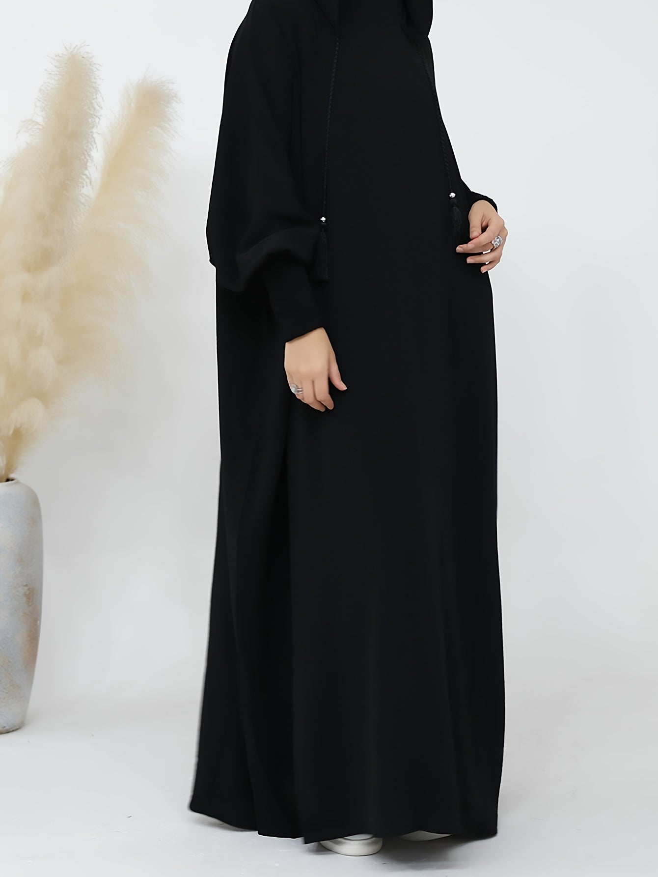 Elegant black abaya with batwing sleeves, drawstring hood, and loose fit. Versatile minimalist style for all seasons. Made of polyester.