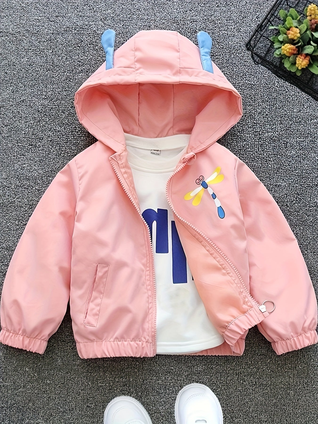 Girls' pink lightweight hooded windbreaker with playful cartoon face design and bow detail. Zip-up style made from polyester blend, perfect for spring and autumn.