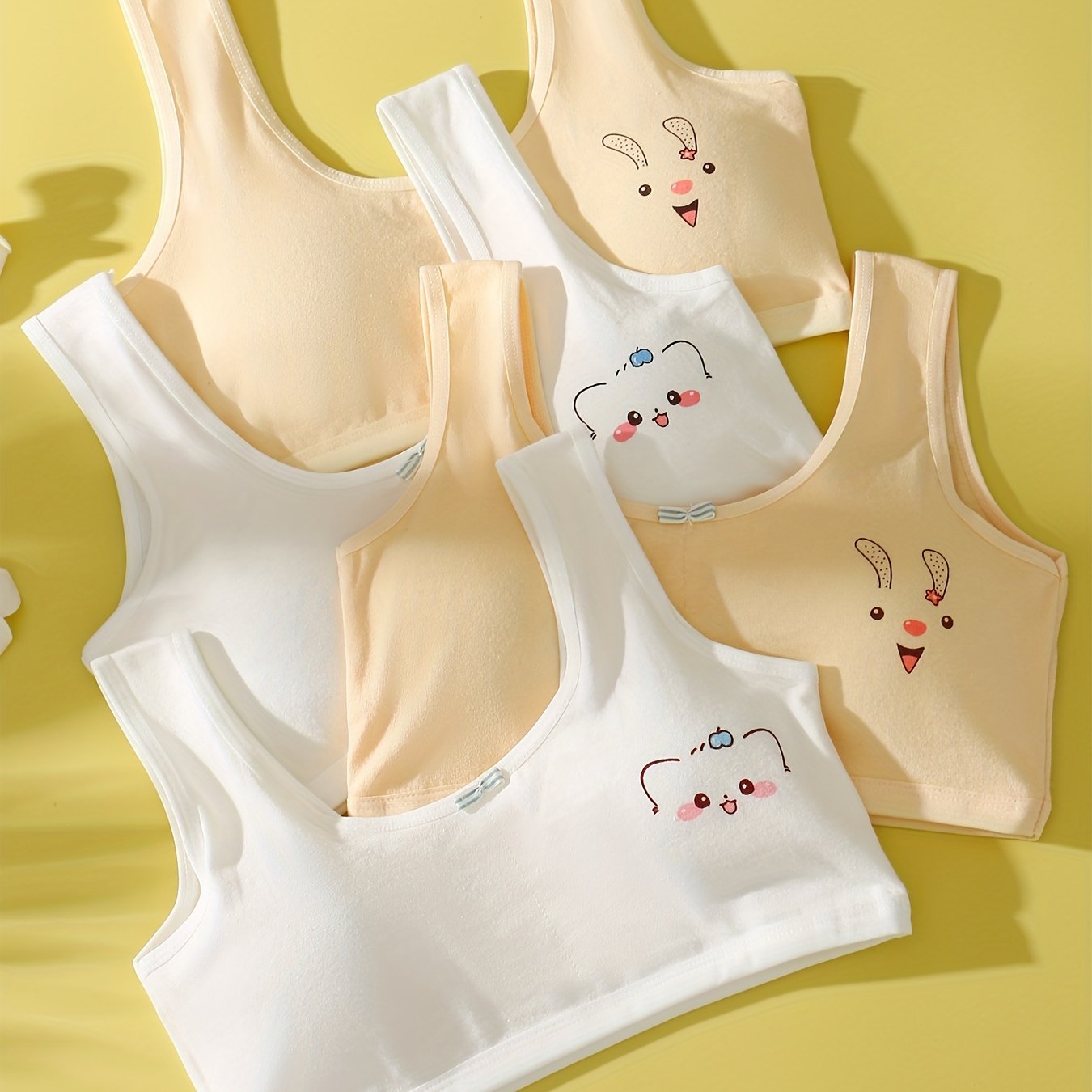 4 comfy cotton bras for girls aged 7-13 with cute animal illustrations in solid colors. Stretchy and machine washable. Includes white, yellow, blue, pink. Ideal for elementary to high