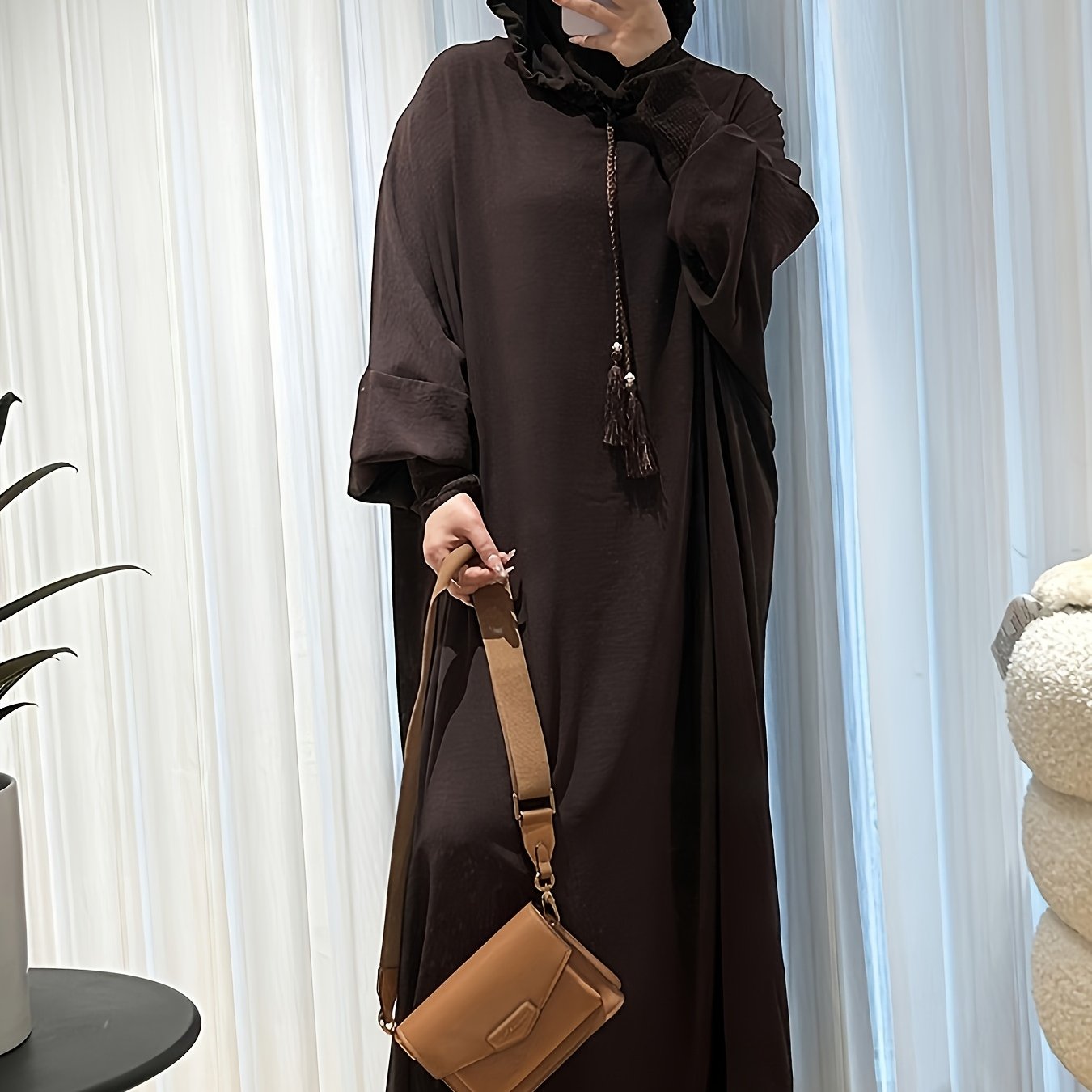 Elegant black abaya with batwing sleeves, drawstring hood, and loose fit. Versatile minimalist style for all seasons. Made of polyester.