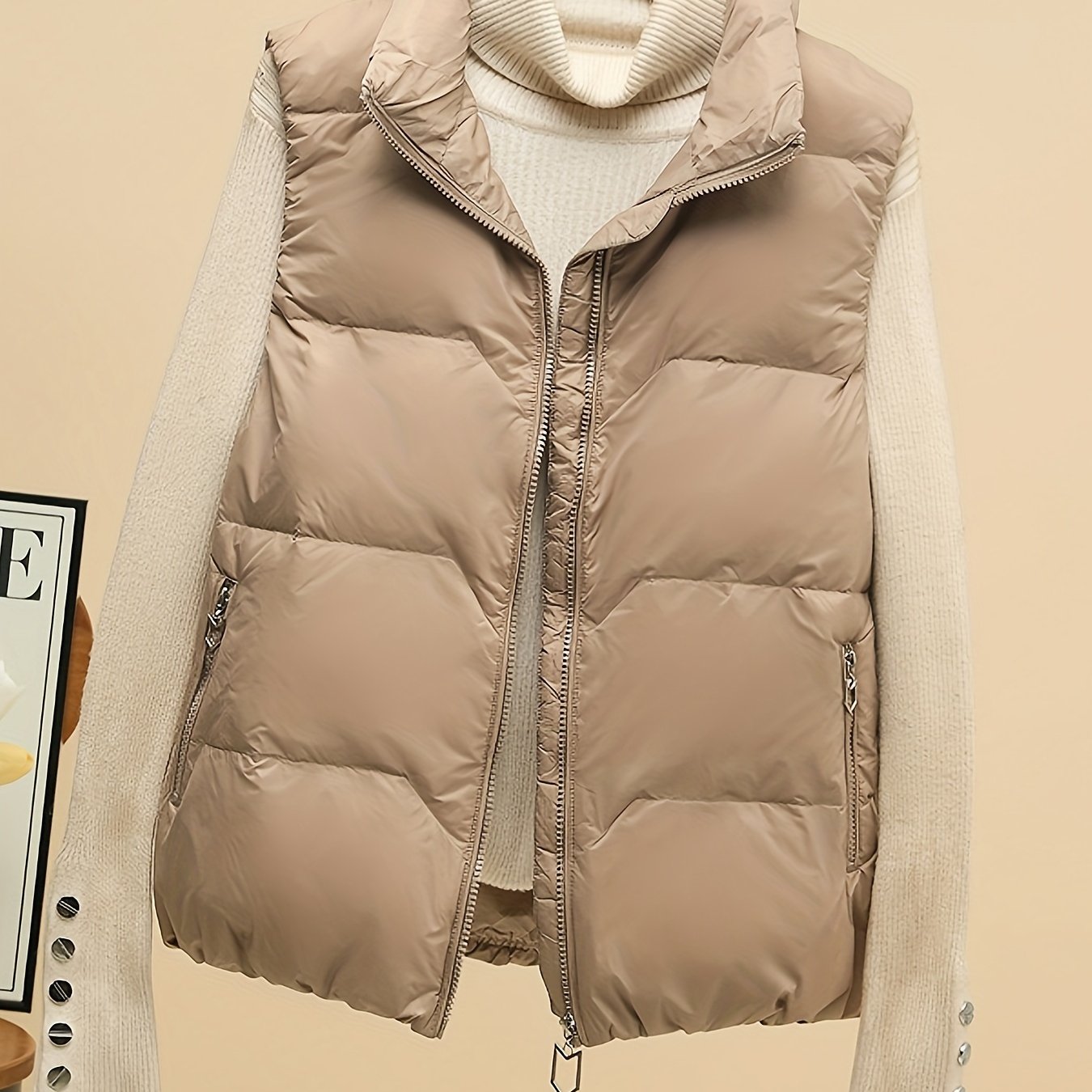 Sleeveless beige duck down vest with side pockets and zip-up closure. Perfect for fall/winter layering with a loose fit and 80g white duck down fill. Made of polyester with a glossy finish.