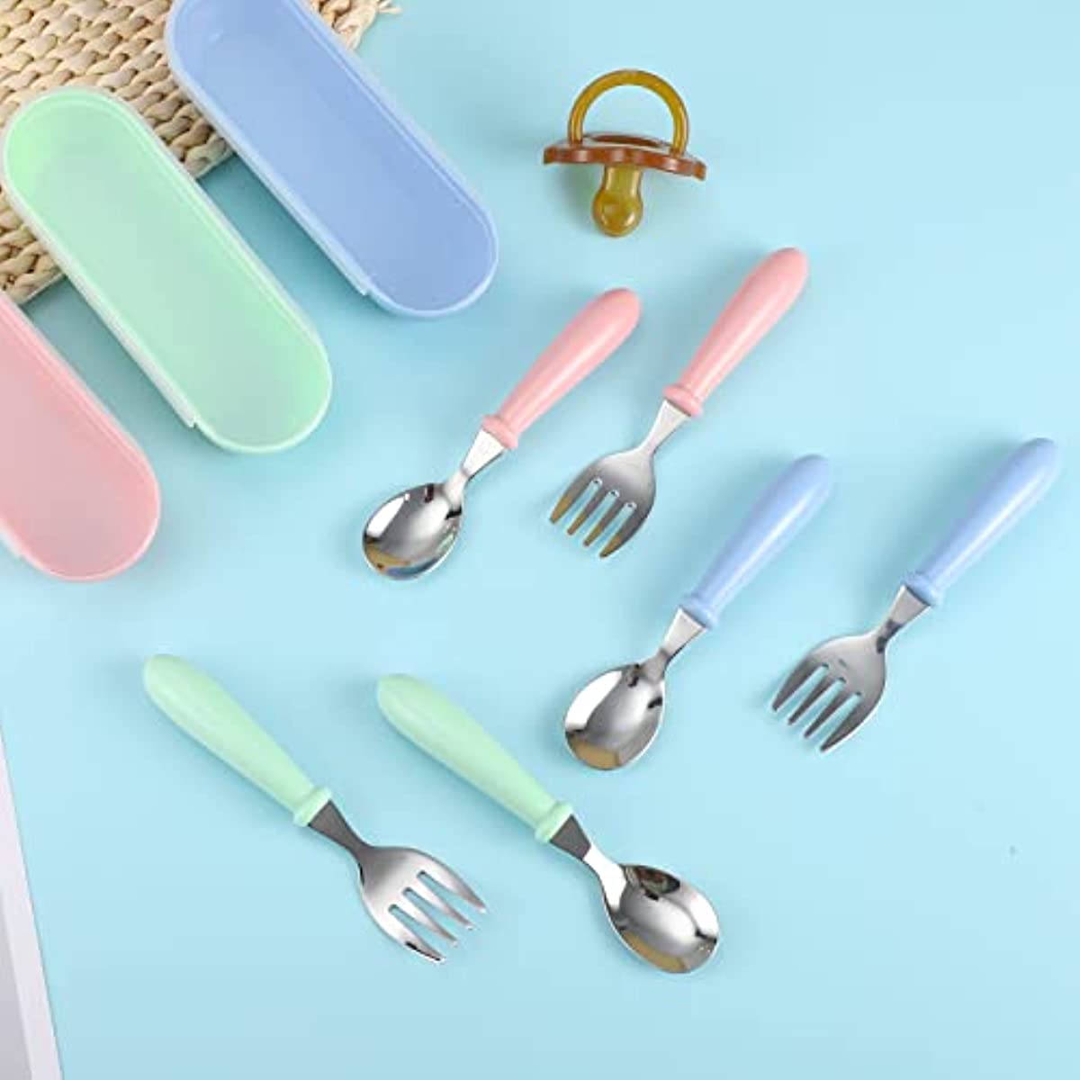 Set of 3 stainless steel youngsters' utensils with colorful handles, dishwasher safe. Includes fork and spoon in blue geometric pattern in pink and green cases.