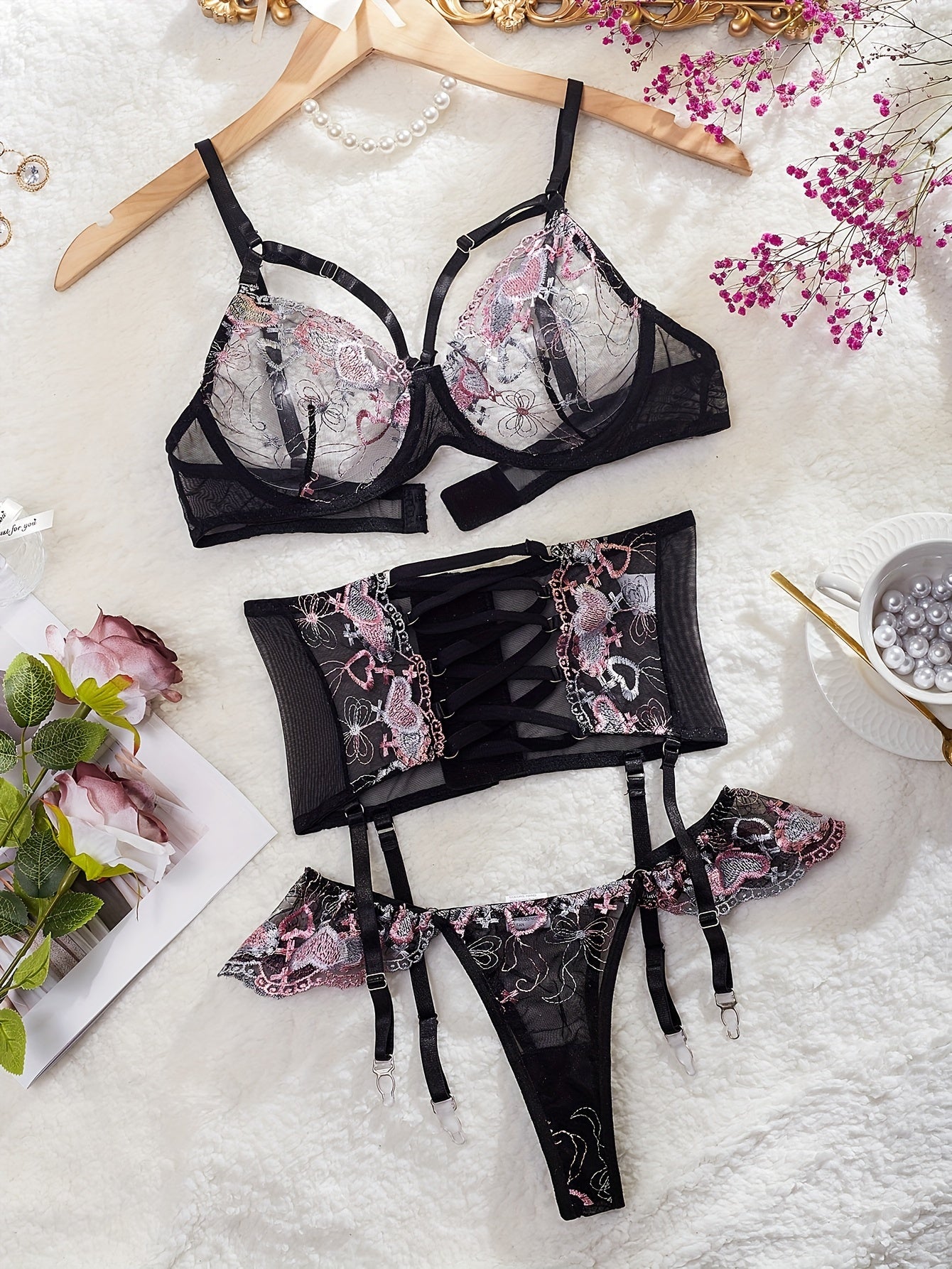 3-Piece lingerie set with heart embroidery, cross strappy detail, sheer mesh material in black with pink accents. Includes bra, garter belt, and thong.