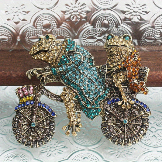 Vintage style rhinestone brooch pin featuring two frogs on a bike, a unique animal design accessory.