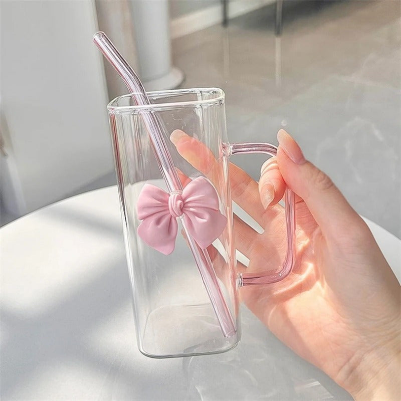 Clear Glass Mug with Handle features a bow decoration on a square drinking cup. This high-temperature resistant mug comes with a straw, perfect for enjoying coffee, milk, or water. Ideal for use at home, in the kitchen, or at parties.