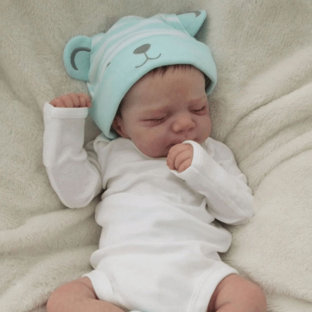 Realistic 18-inch reborn girl doll with blue bear hat, soft vinyl body, detailed skin, visible veins, and lifelike sleeping pose. Ideal birthday gift for children 3 and up.