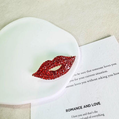 Two pieces of a sexy red lip brooch adorned with sparkling diamonds, creating a fashionable and luxurious accessory for high-end clothing.