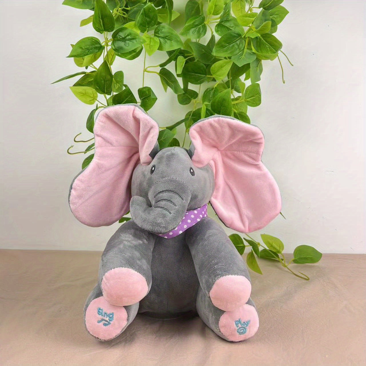 Bright pink and blue interactive elephant plush toy featuring a hide-and-seek game. This singing musical bear doll is designed for girls over 6 years old. Battery operated (AA batteries not included).