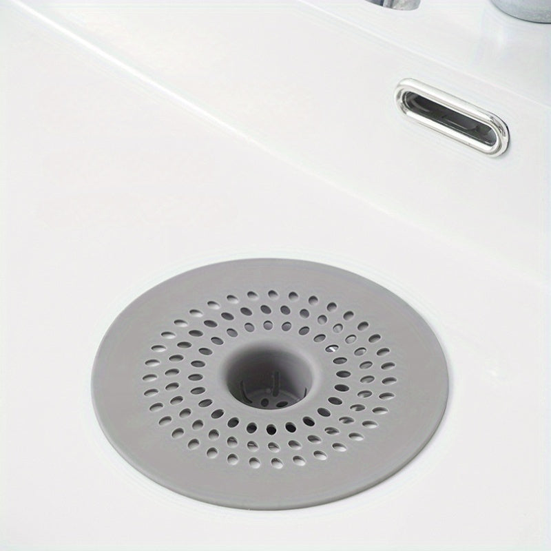 Silicone drain strainer with circular design for shower and kitchen sinks. Available in black or white. Easy to install with drain holes. Ideal for bathroom or kitchen use.