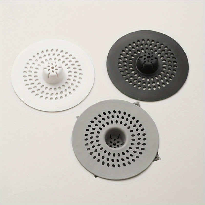 Silicone drain strainer with circular design for shower and kitchen sinks. Available in black or white. Easy to install with drain holes. Ideal for bathroom or kitchen use.