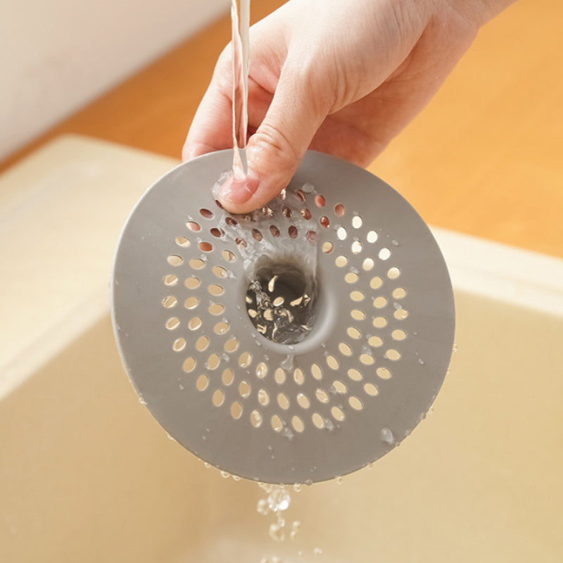 Silicone drain strainer with circular design for shower and kitchen sinks. Available in black or white. Easy to install with drain holes. Ideal for bathroom or kitchen use.