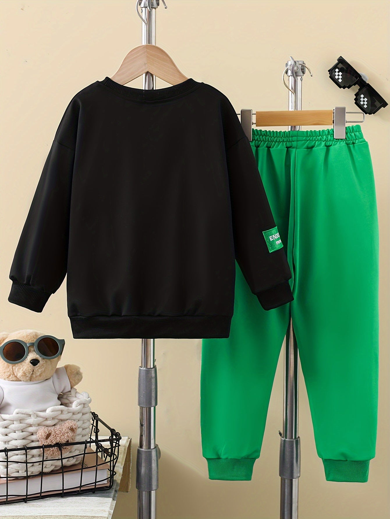 Boys' two-piece suit for outdoor wear with bear print hat, black sweatshirt, and green letter logo trousers.