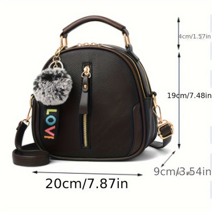 Large capacity women's handbag in brown and gray with golden-tone hardware, adjustable strap, and zipper closure. Features pom pom charm and casual yet trendy design.