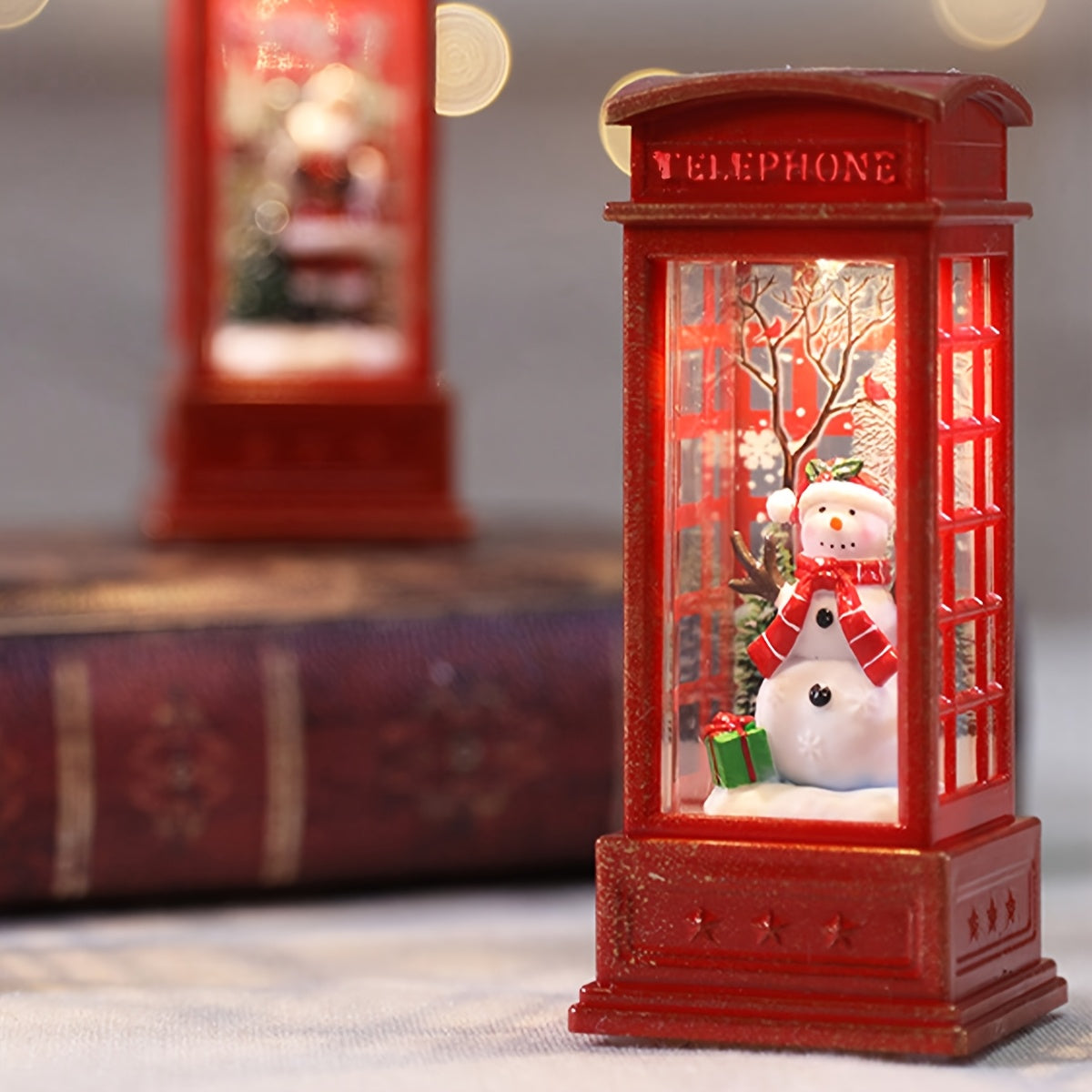 Festive Christmas phone booth decoration featuring Santa, snowman, and tree scenes. Battery-operated with illuminated red cabinet for holiday display.