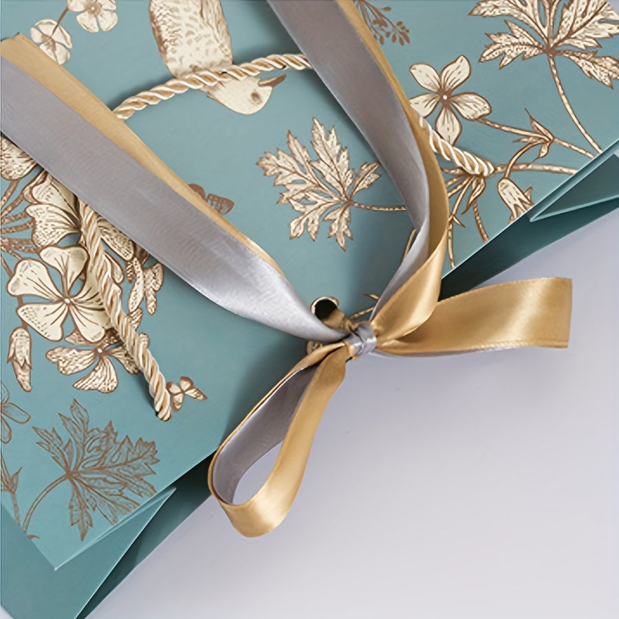 Floral paper gift bag with golden ribbon, teal background, brown, white & gray flowers, suitable for birthdays, weddings, Mother's Day, and special occasions. Features drawstring closure.