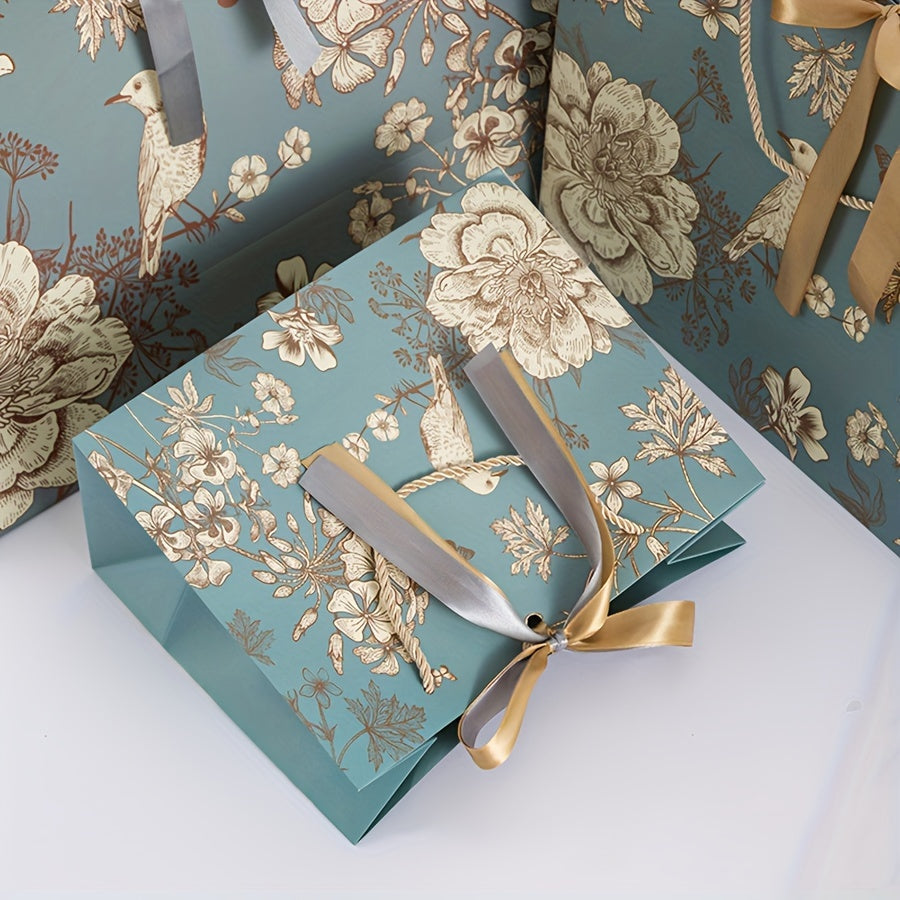 Floral paper gift bag with golden ribbon, teal background, brown, white & gray flowers, suitable for birthdays, weddings, Mother's Day, and special occasions. Features drawstring closure.