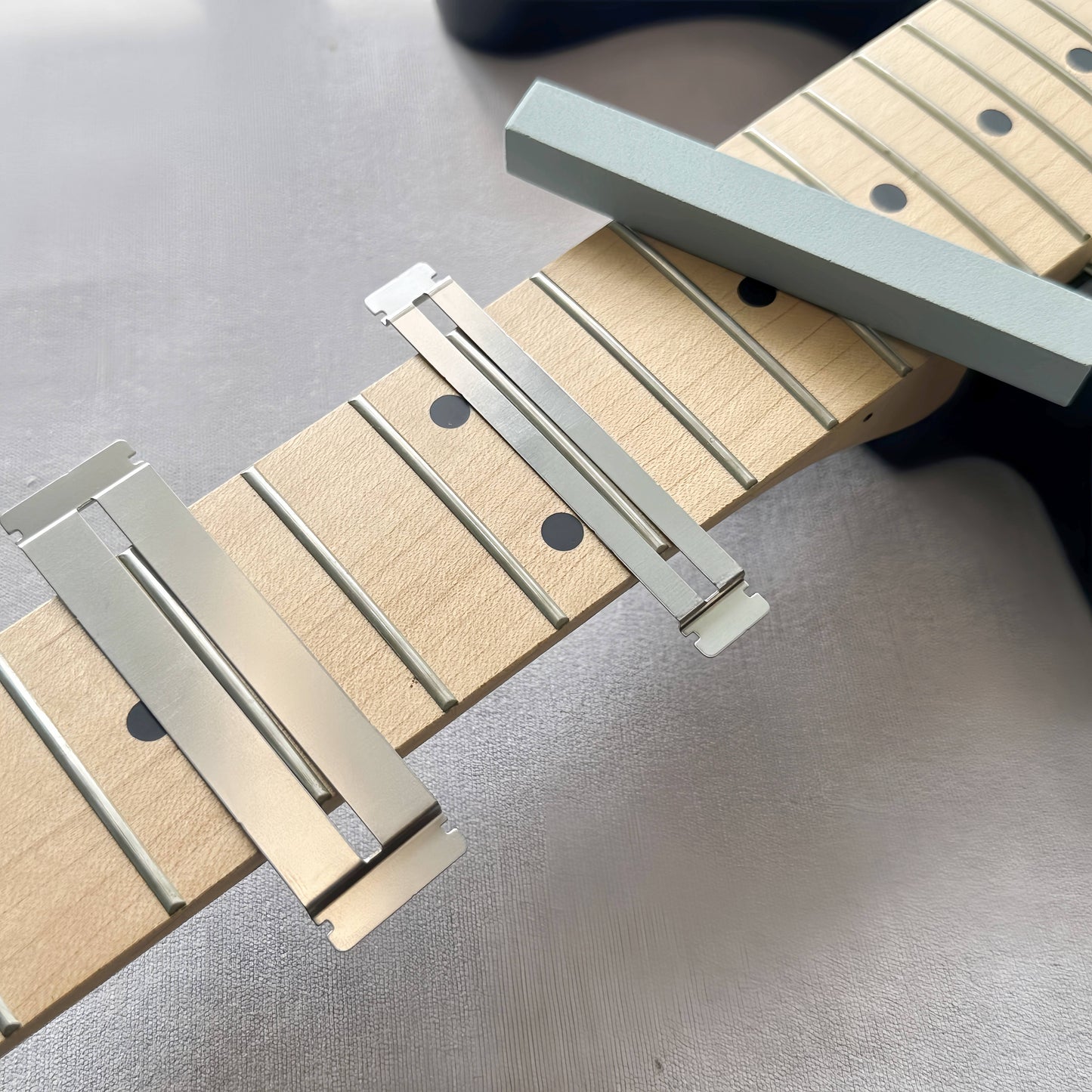 Guitar fretboard maintenance kit with metal protector and grey dressing stones for various string instruments.