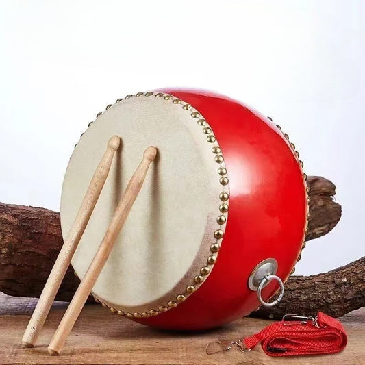 Red cowhide drum with white rivets, durable plastic body, wooden drumsticks & carrying strap included. Ideal for beginners and enthusiasts, essential for stage performances. Riveted design