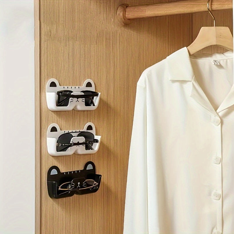 Wall-mounted whimsical cat eyeglass holder made of punch-free plastic, designed to store and display glasses in a space-saving and fashionable manner.