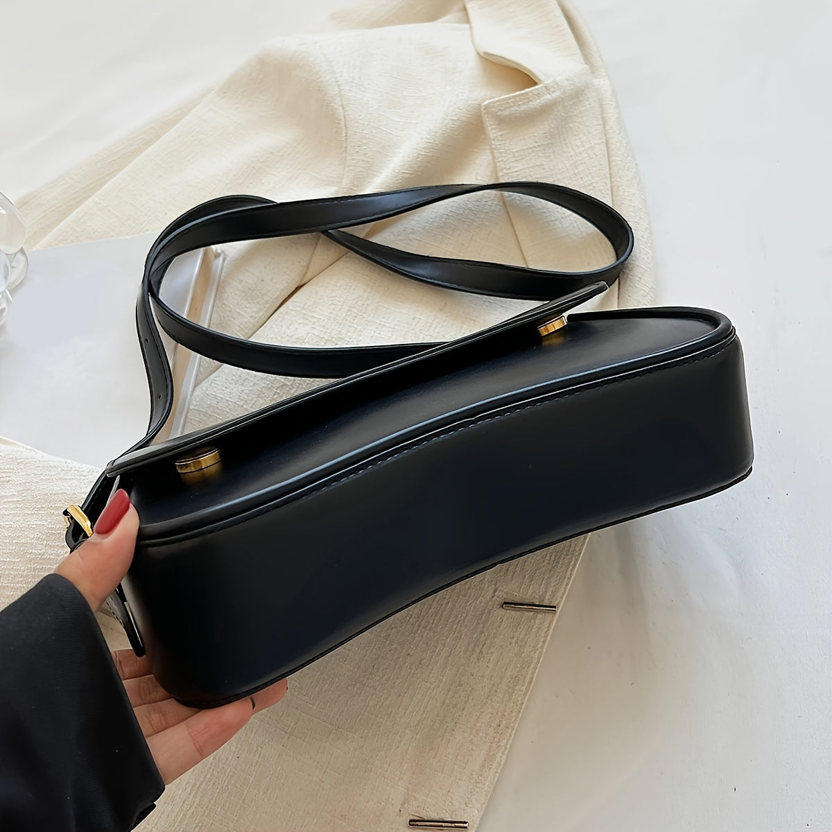 Stylish black baguette bag with adjustable strap, textured flap design, and goldtone hardware. Ideal formal accessory for women.