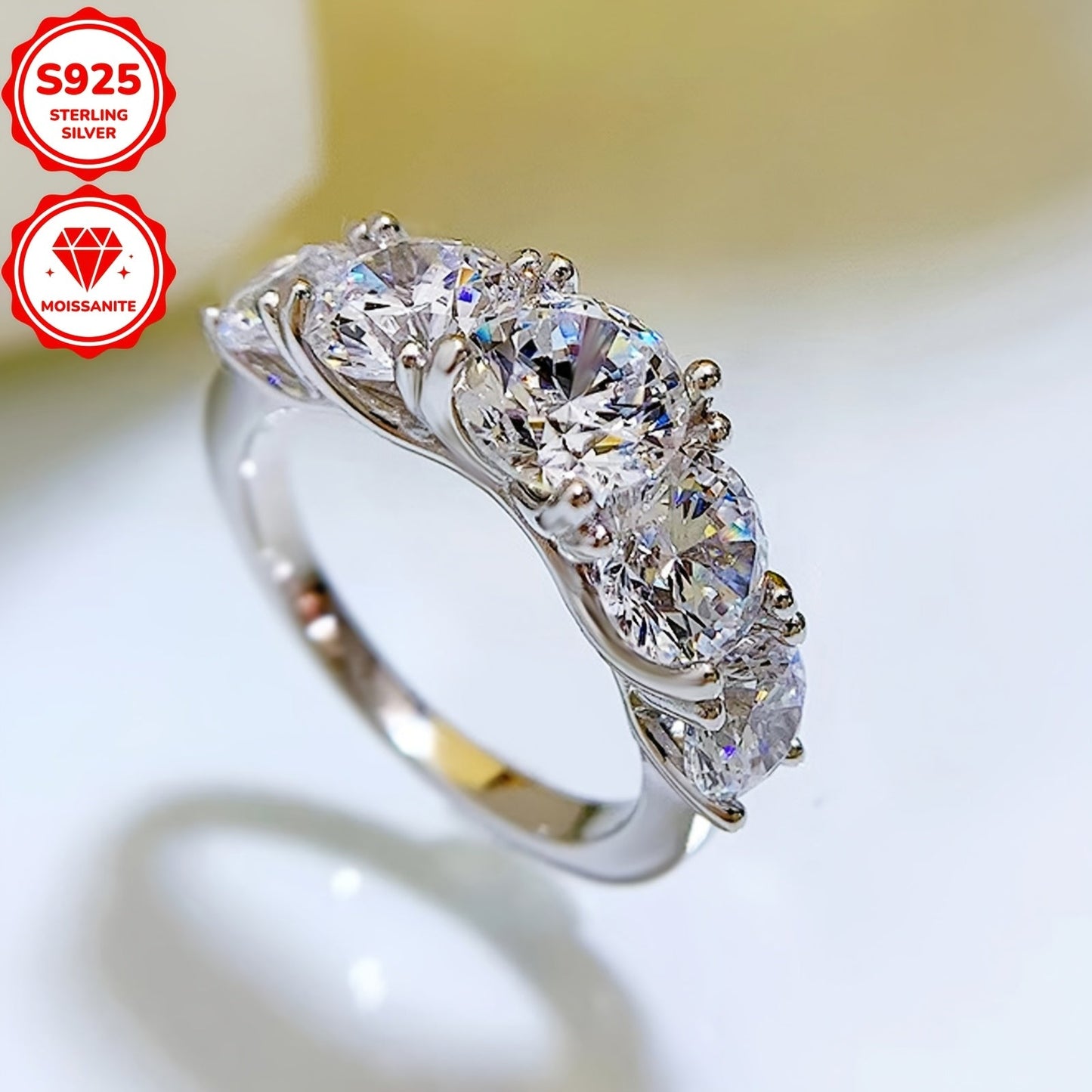 Ushbu ayollar uchun uzuk 925 sterling kumushdan tayyorlangan bo'lib, go'zal moissanite toshlari bilan bezatilgan. Uzukda 6.5mm markaziy tosh, ikkita 6mm tosh va ikkita 5mm tosh mavjud bo'lib, jami 3.60ct. Har bir tosh ehtiyotkorlik bilan o'rnatilgan.