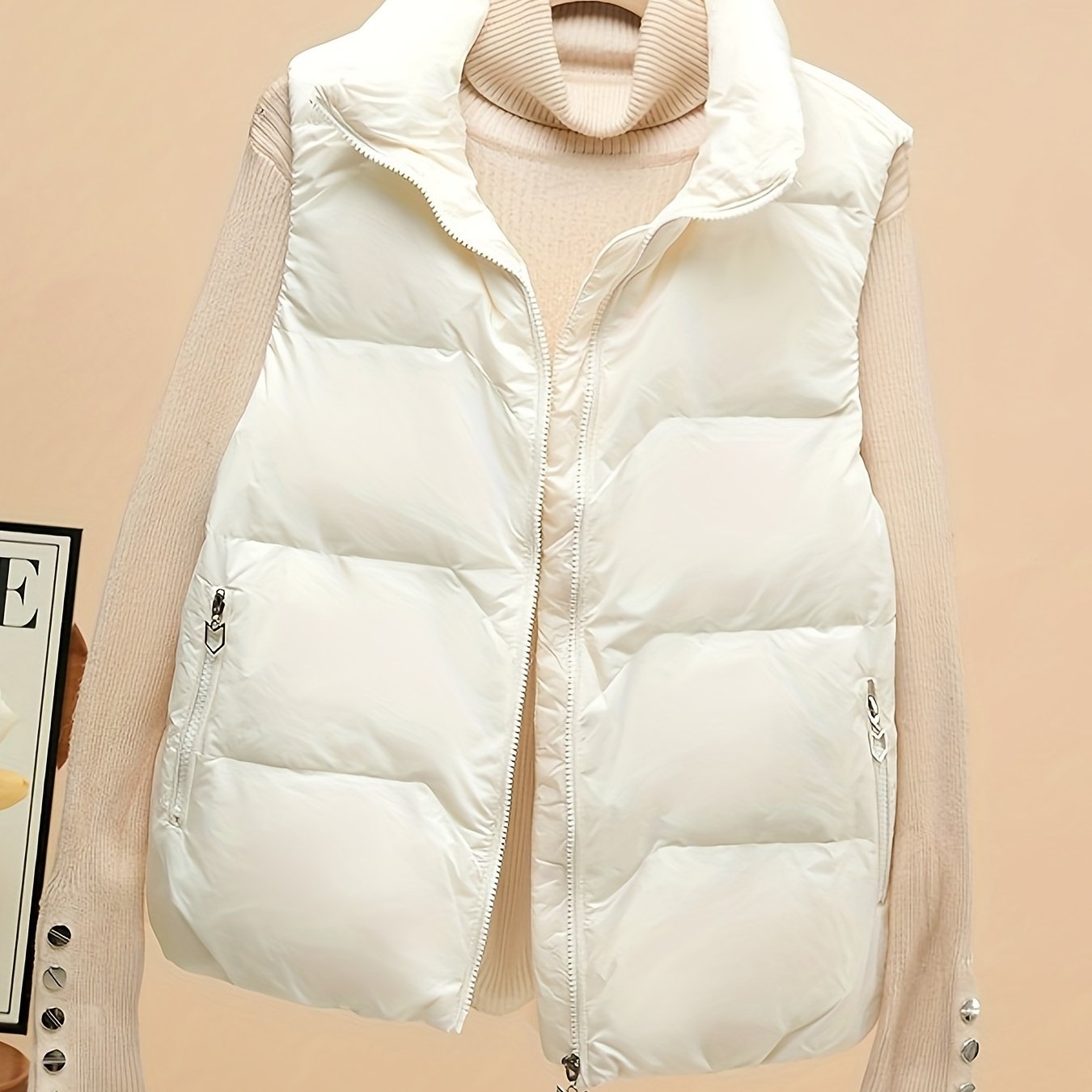 Sleeveless beige duck down vest with side pockets and zip-up closure. Perfect for fall/winter layering with a loose fit and 80g white duck down fill. Made of polyester with a glossy finish.