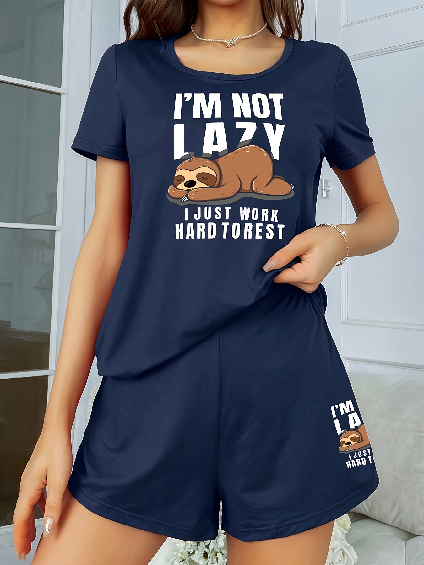 Women's sleepwear set with cute sloth print and slogan, including short sleeve top and elastic shorts.