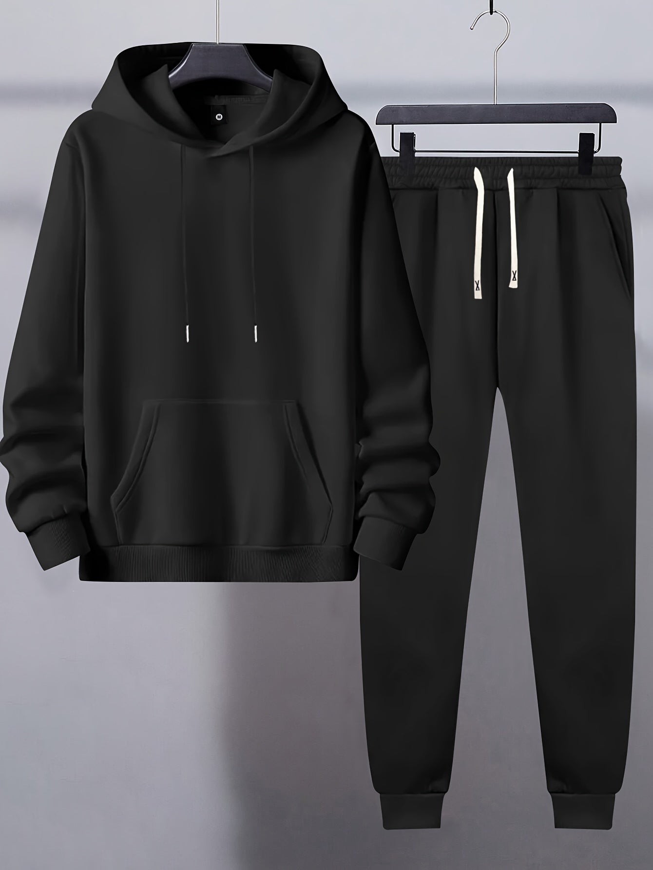 Men's basic polyester sweatsuit set includes a solid color hooded sweatshirt and drawstring joggers with pockets. Made of knit fabric with slight stretch, it has long sleeves and a regular