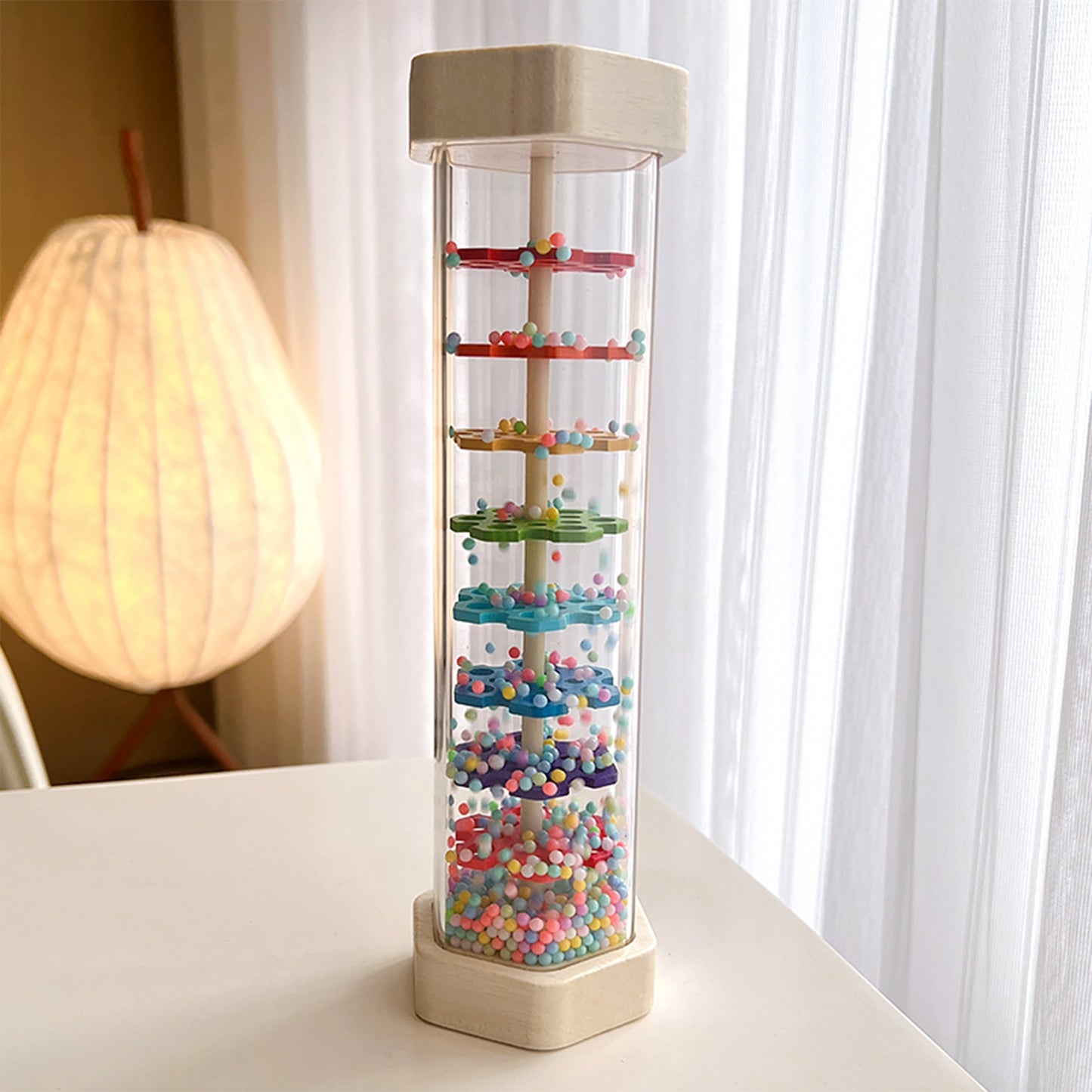 Musical instrument for babies that simulates the soothing sound of rain in a wooden tube, similar to a rainbow hourglass sandbell.