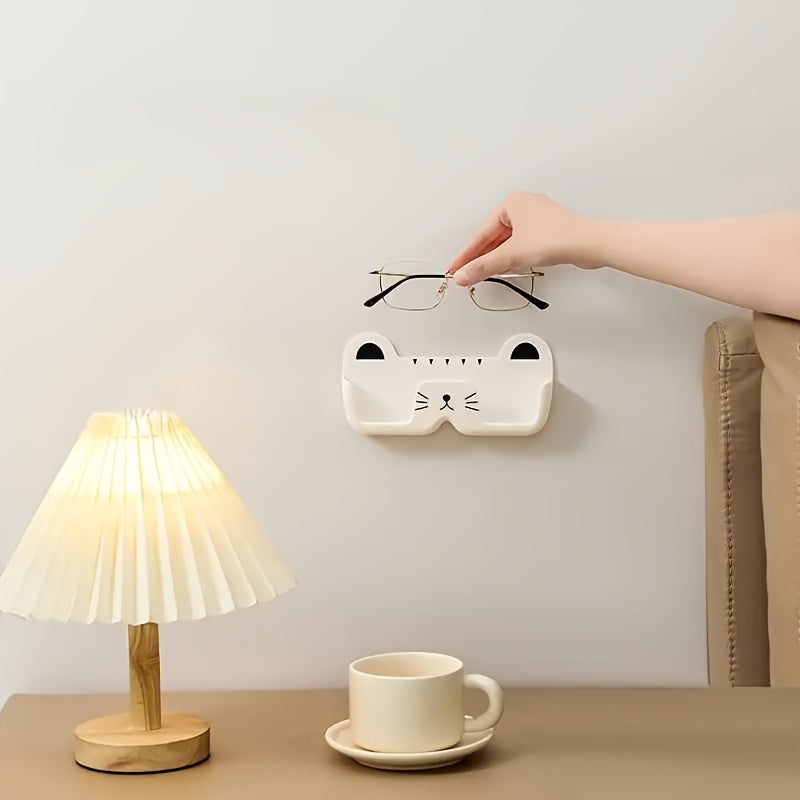 Wall-mounted whimsical cat eyeglass holder made of punch-free plastic, designed to store and display glasses in a space-saving and fashionable manner.