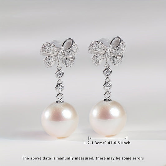 These women's fashionable dangling earrings feature a pair of 12-13mm large grains of strong light, slightly flawed round natural freshwater pearls set in S925 silver. Each earring is adorned with a delicate bow and comes in a gift box. Please note that