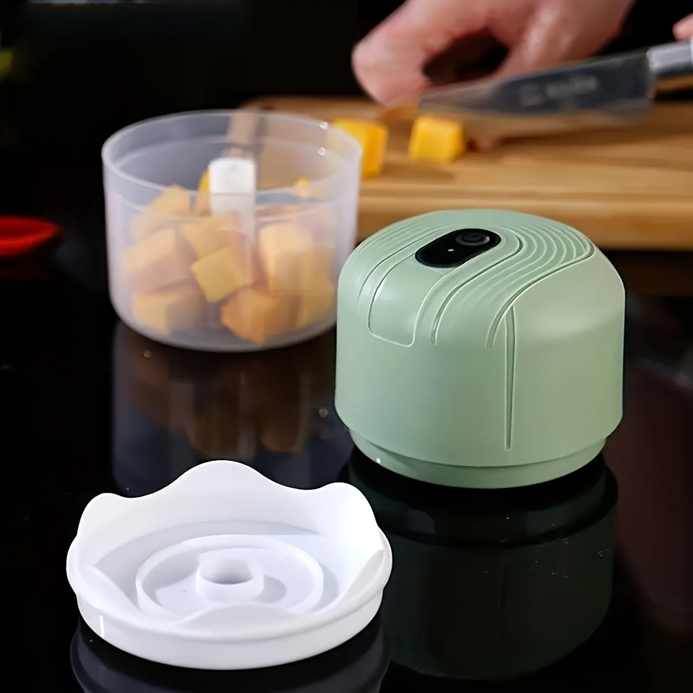 Round plastic container containing a portable multifunctional food chopper that is USB rechargeable. This versatile appliance can be used as a vegetable dicer, garlic masher, manual food processor, and electric mini kitchen appliance with a lithium