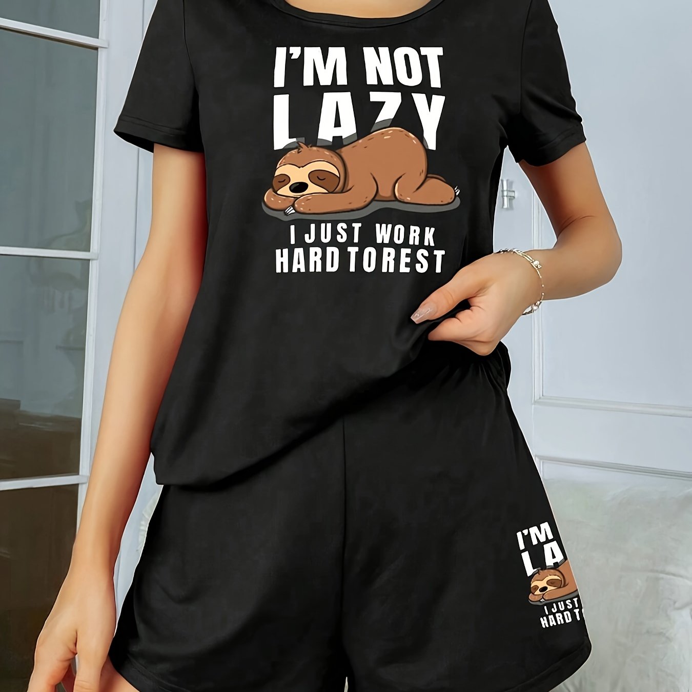 Women's sleepwear set with cute sloth print and slogan, including short sleeve top and elastic shorts.