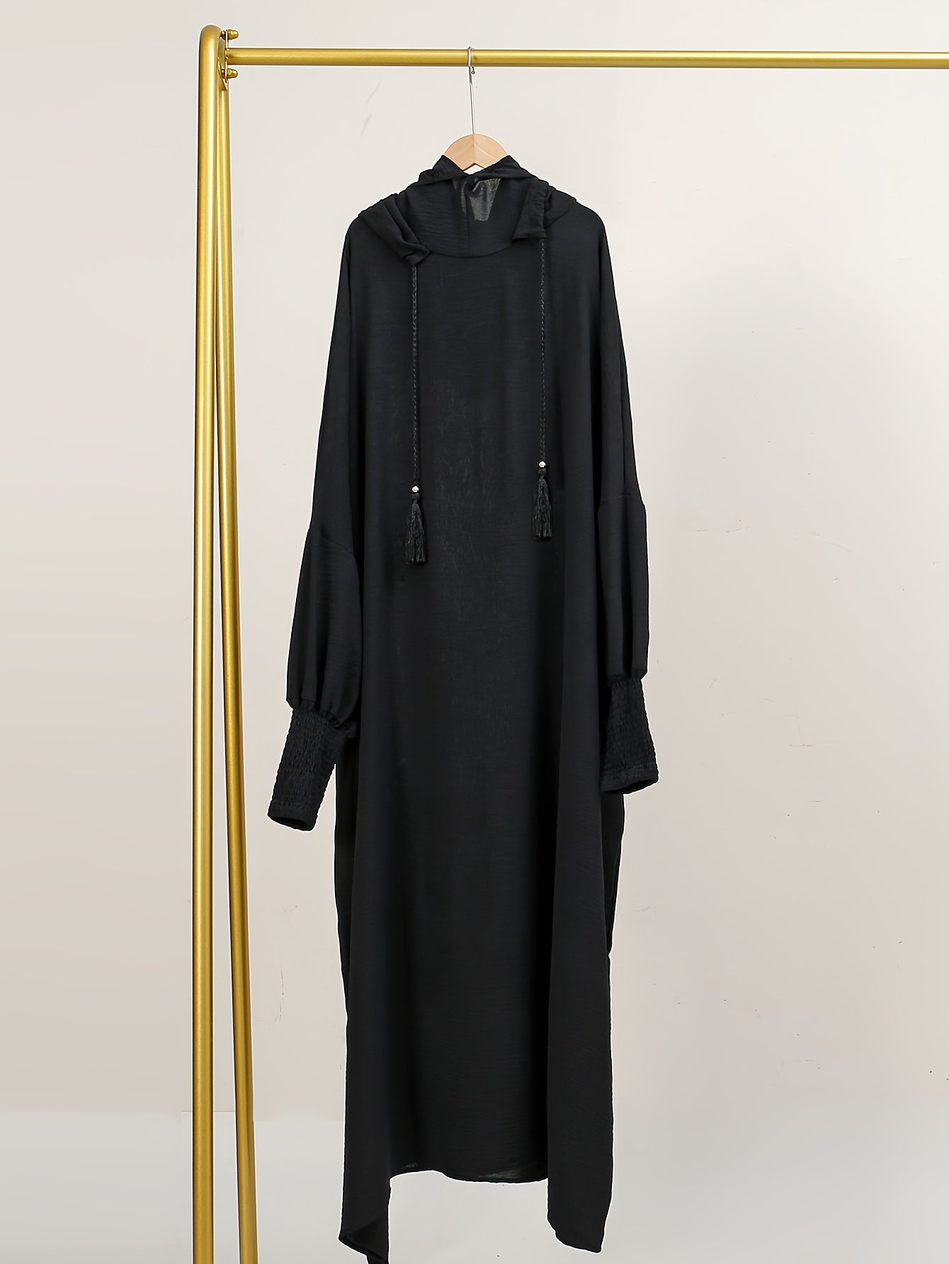 Elegant black abaya with batwing sleeves, drawstring hood, and loose fit. Versatile minimalist style for all seasons. Made of polyester.