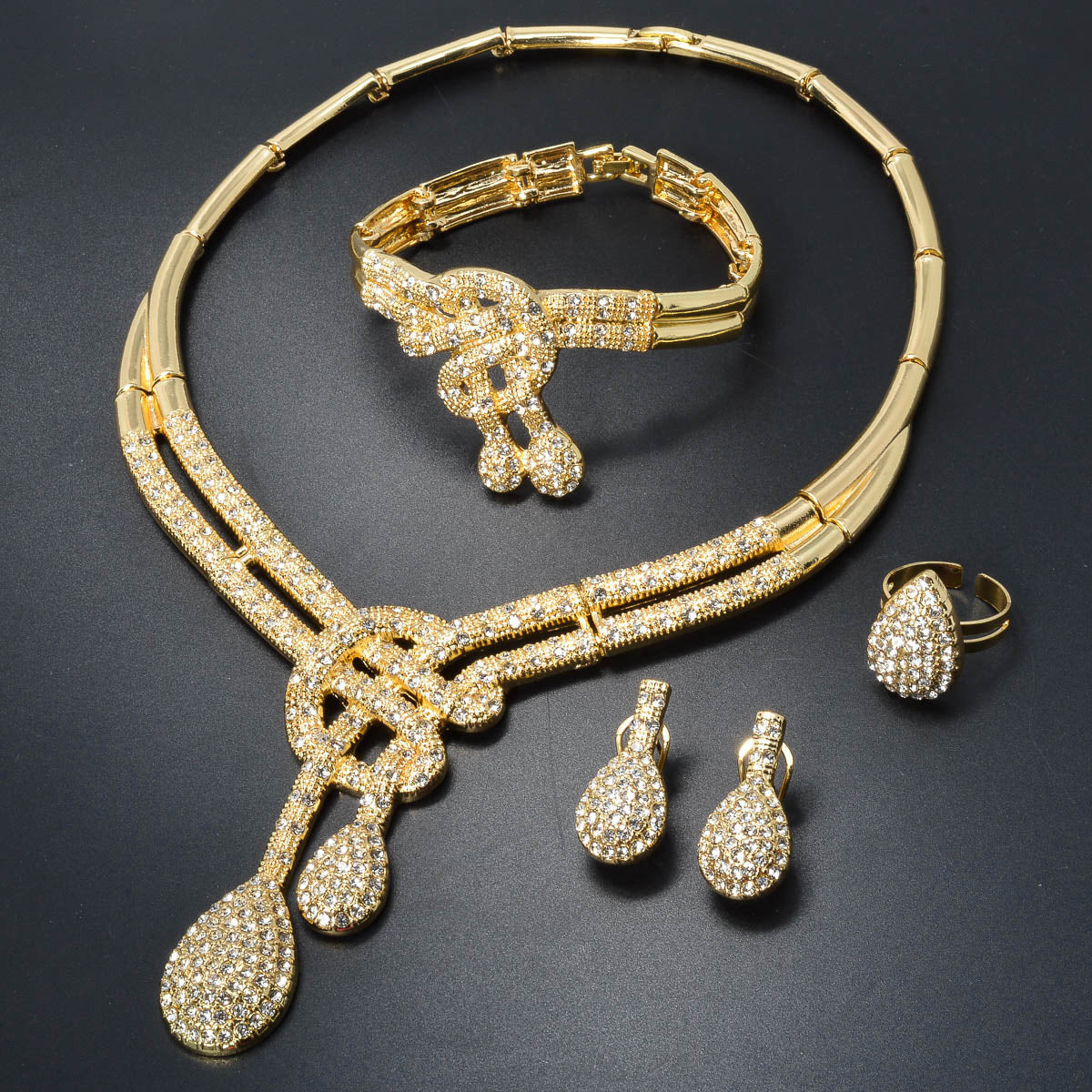 Vintage jewelry set featuring elegant geometric and musical note designs with tassel accents. Made with synthetic cubic zirconia and copper materials. Set includes a necklace, bracelet, earrings, and ring. Perfect for adding a touch of luxury sparkle to