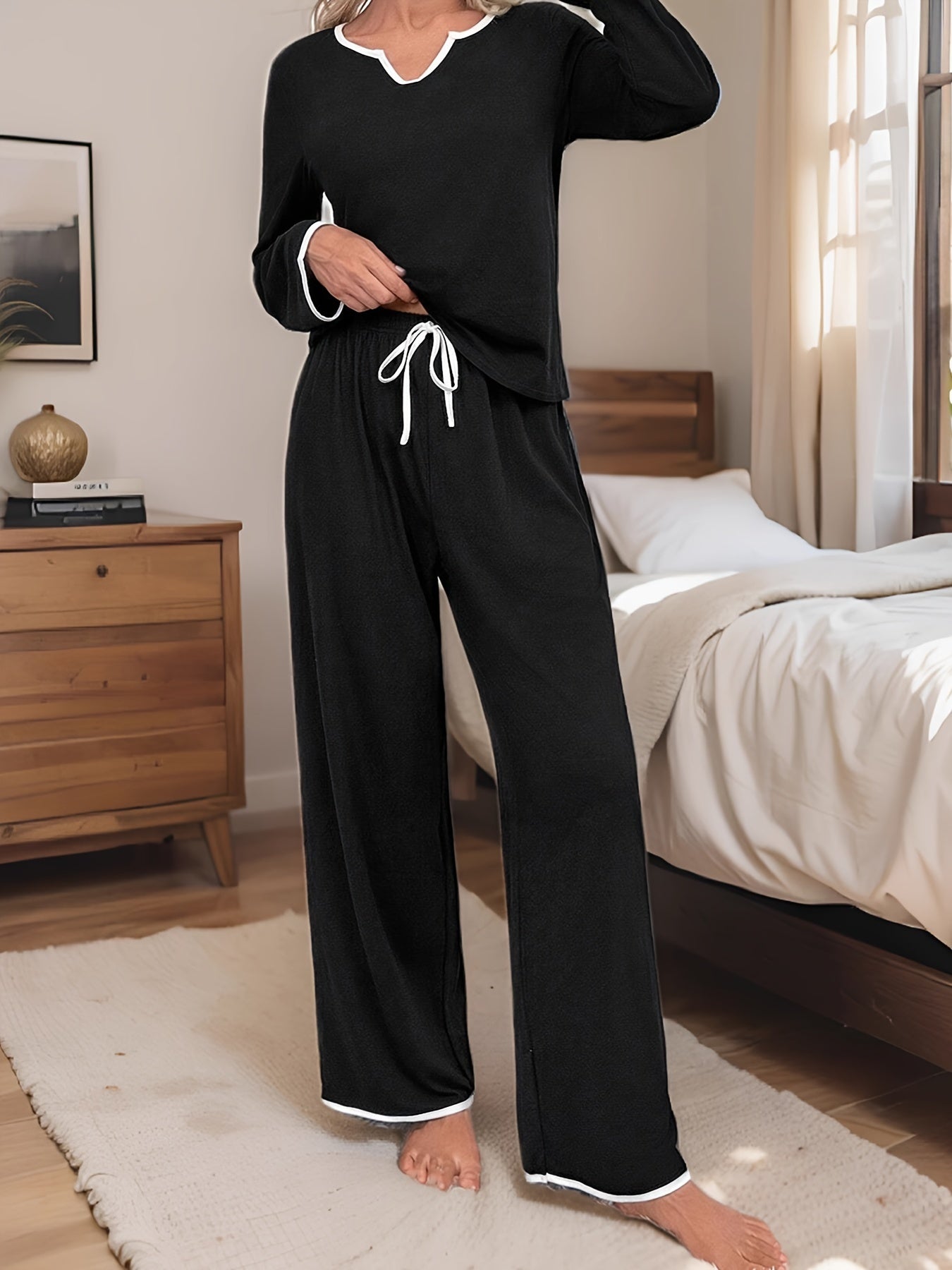 Soft polyester blend pajama set in black with white contrast trim, featuring long sleeve top and elastic waist pants with tie front for ultimate comfort and style. Perfect for cozy