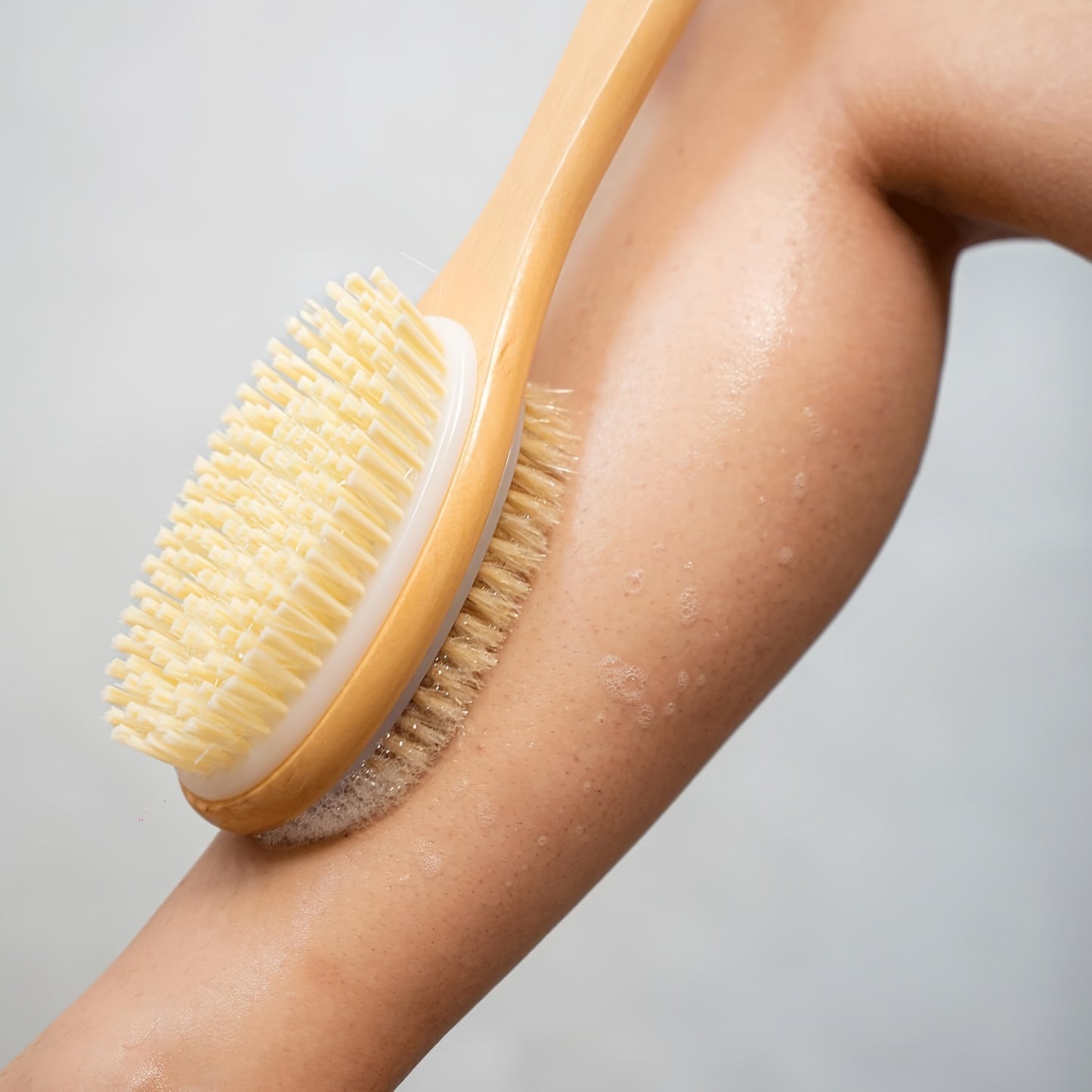 Long-handled dual-sided shower brush for deep cleaning and exfoliating, suitable for lotion application without needing power.