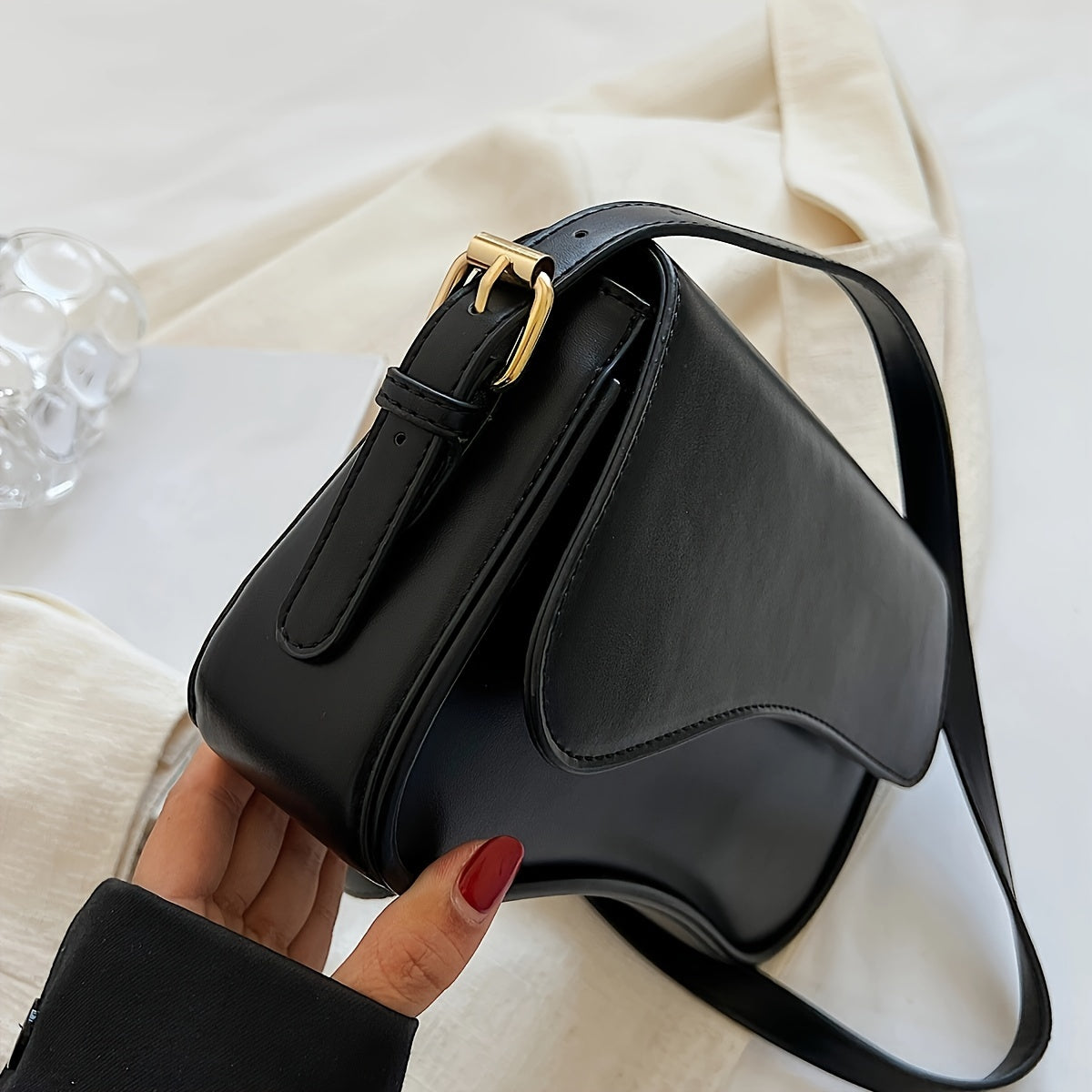 Stylish black baguette bag with adjustable strap, textured flap design, and goldtone hardware. Ideal formal accessory for women.