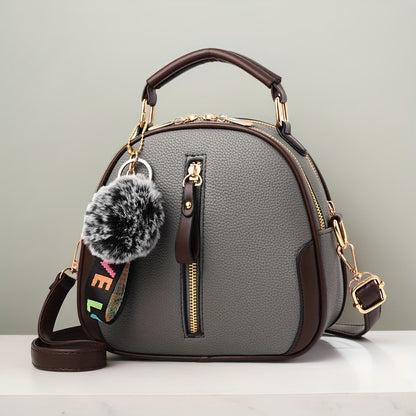 Large capacity women's handbag in brown and gray with golden-tone hardware, adjustable strap, and zipper closure. Features pom pom charm and casual yet trendy design.