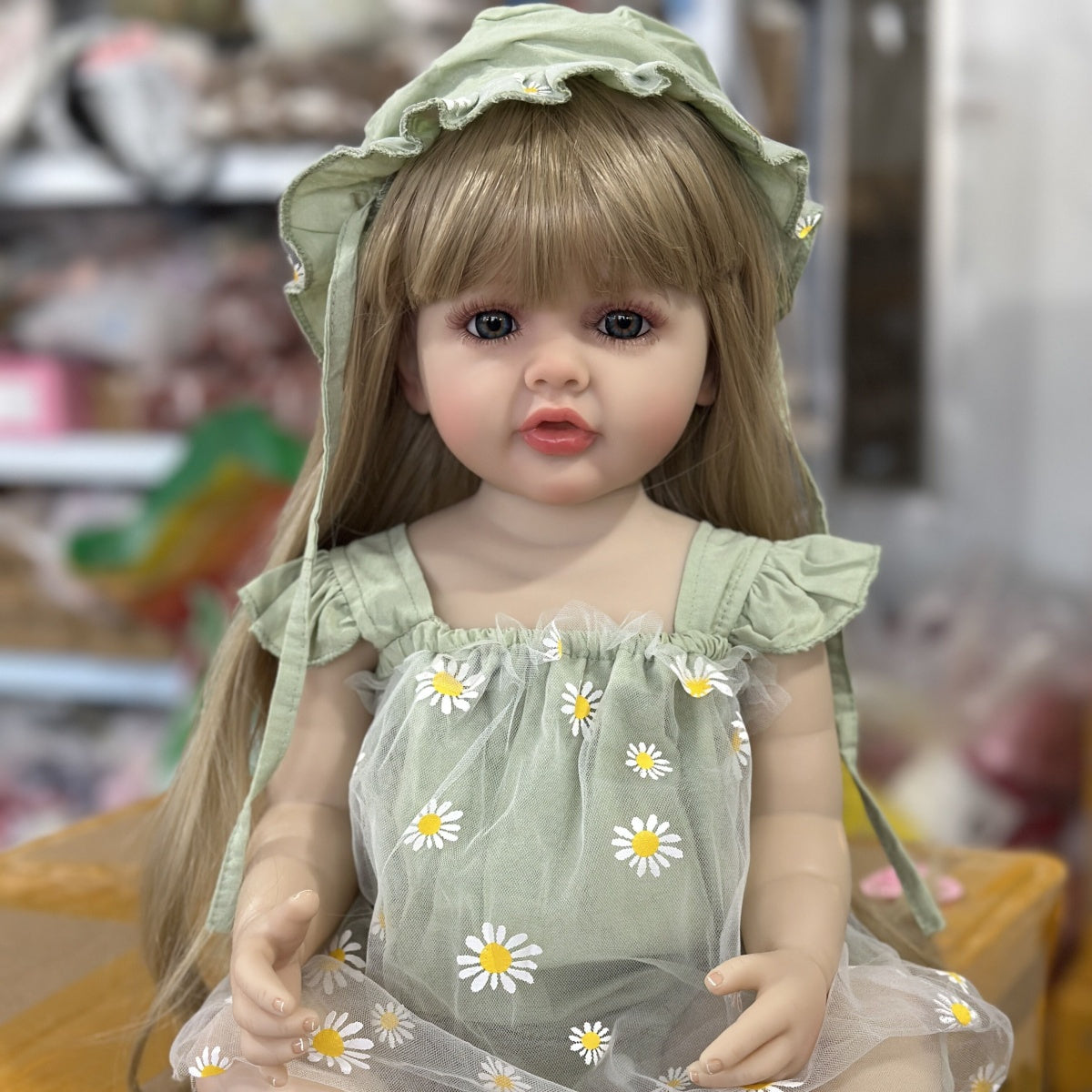 Realistic 55.88 cm full vinyl body reborn baby doll with long blond hair, dressed in a green dress with daisy pattern. Beautiful toddler doll toy for collectors.