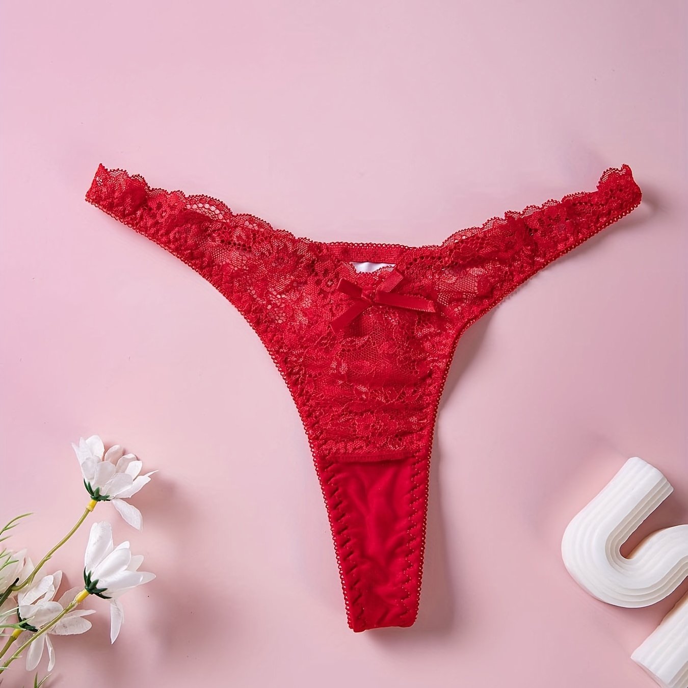 Red lace thong panties with floral print and bow detail, low rise V-shaped design. Made of breathable polyester blend, hand washable. Ideal for intimate moments.