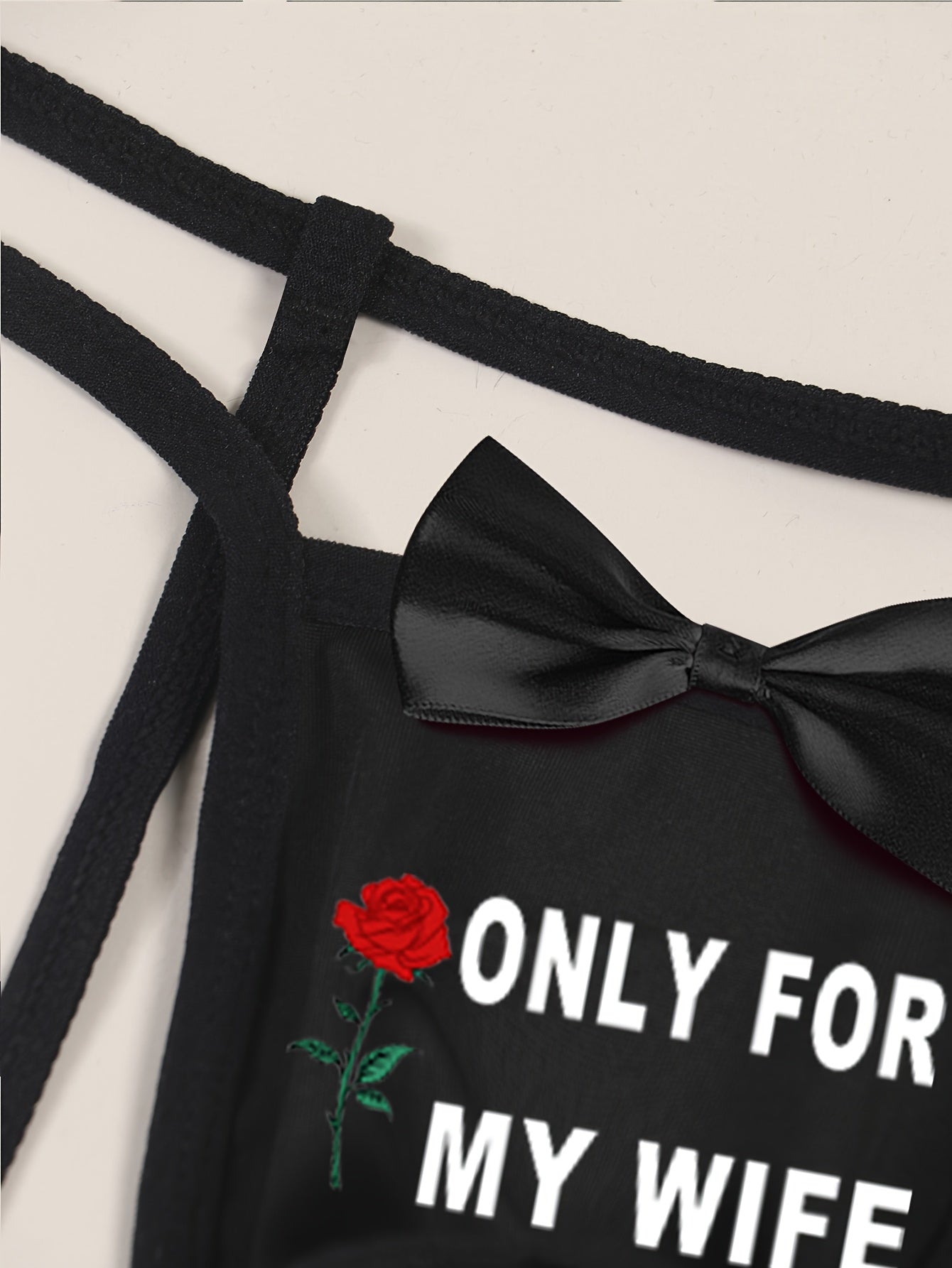 Men's sexy black thong with front cut-out and bow detail, featuring "ONLY FOR MY WIFE" red rose print. Made with comfortable, breathable polyamide (90%) and elastane (10%) knit fabric.