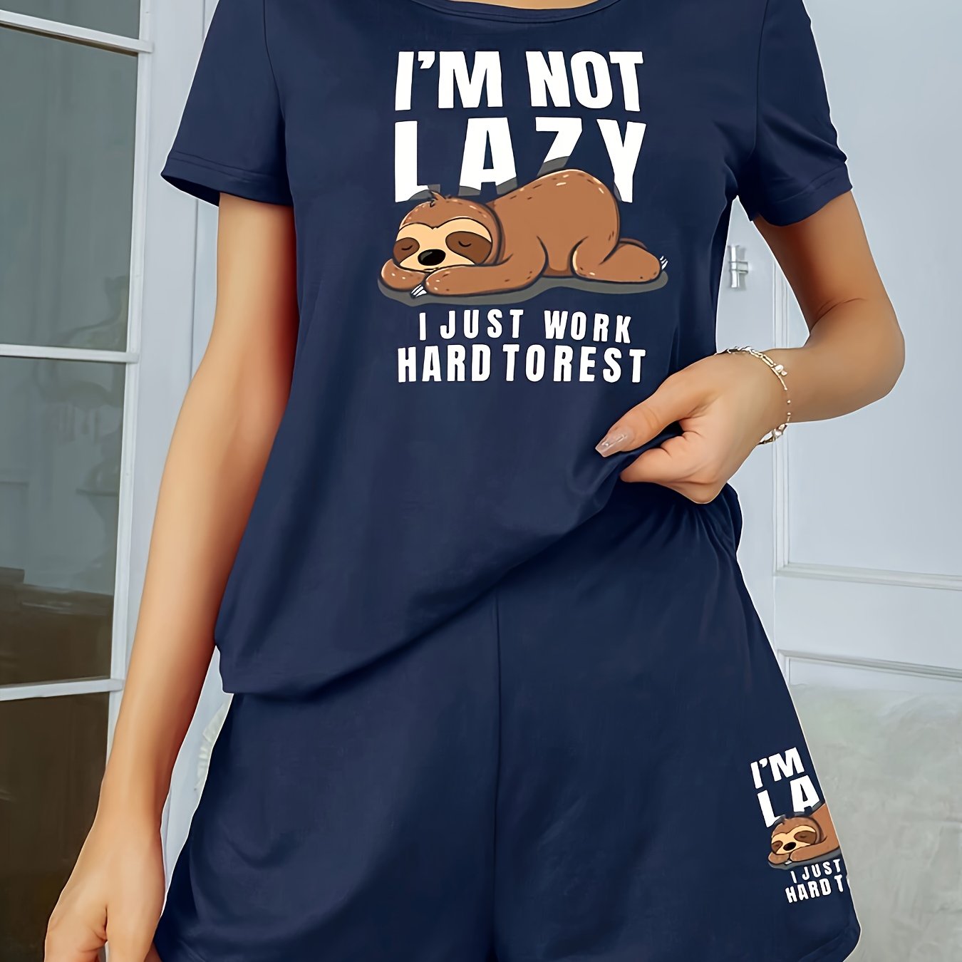 Women's sleepwear set with cute sloth print and slogan, including short sleeve top and elastic shorts.