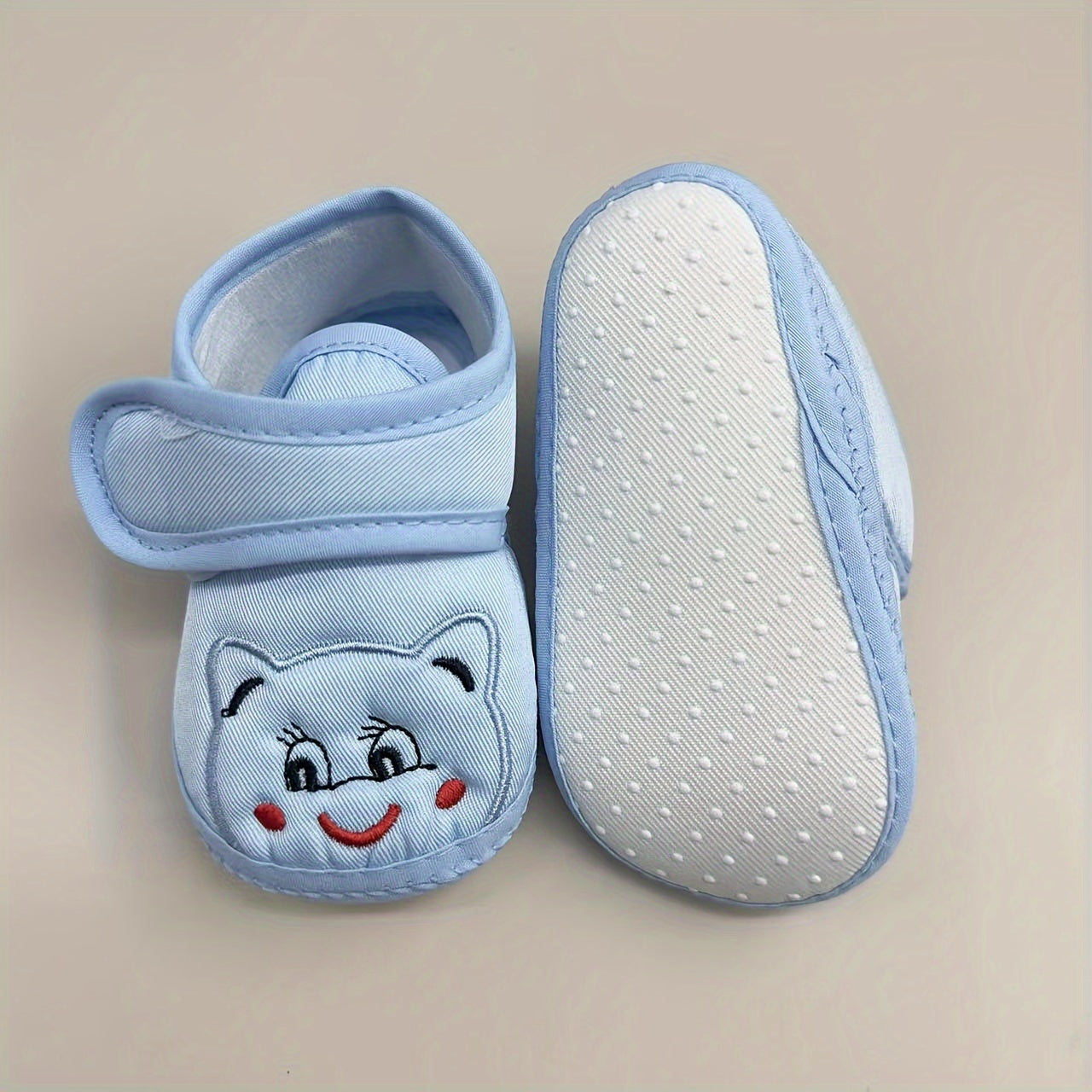 Cute baby walking shoes for boys and girls in light blue with cartoon faces, non-slip soles, and hook-and-loop closure. Ideal for first steps in any season.