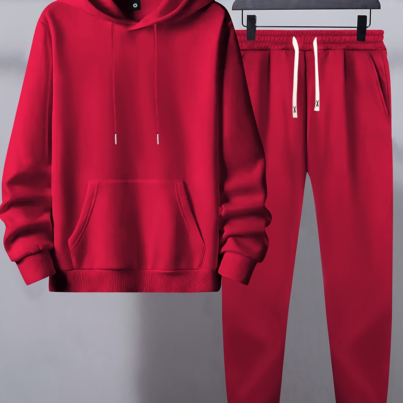 Men's basic polyester sweatsuit set includes a solid color hooded sweatshirt and drawstring joggers with pockets. Made of knit fabric with slight stretch, it has long sleeves and a regular