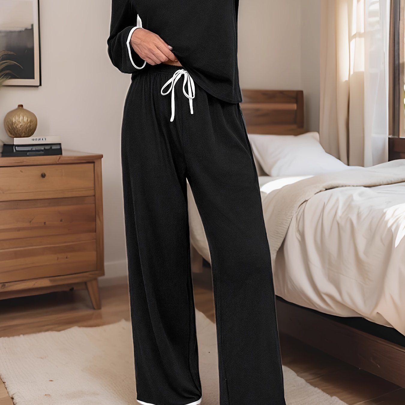 Soft polyester blend pajama set in black with white contrast trim, featuring long sleeve top and elastic waist pants with tie front for ultimate comfort and style. Perfect for cozy