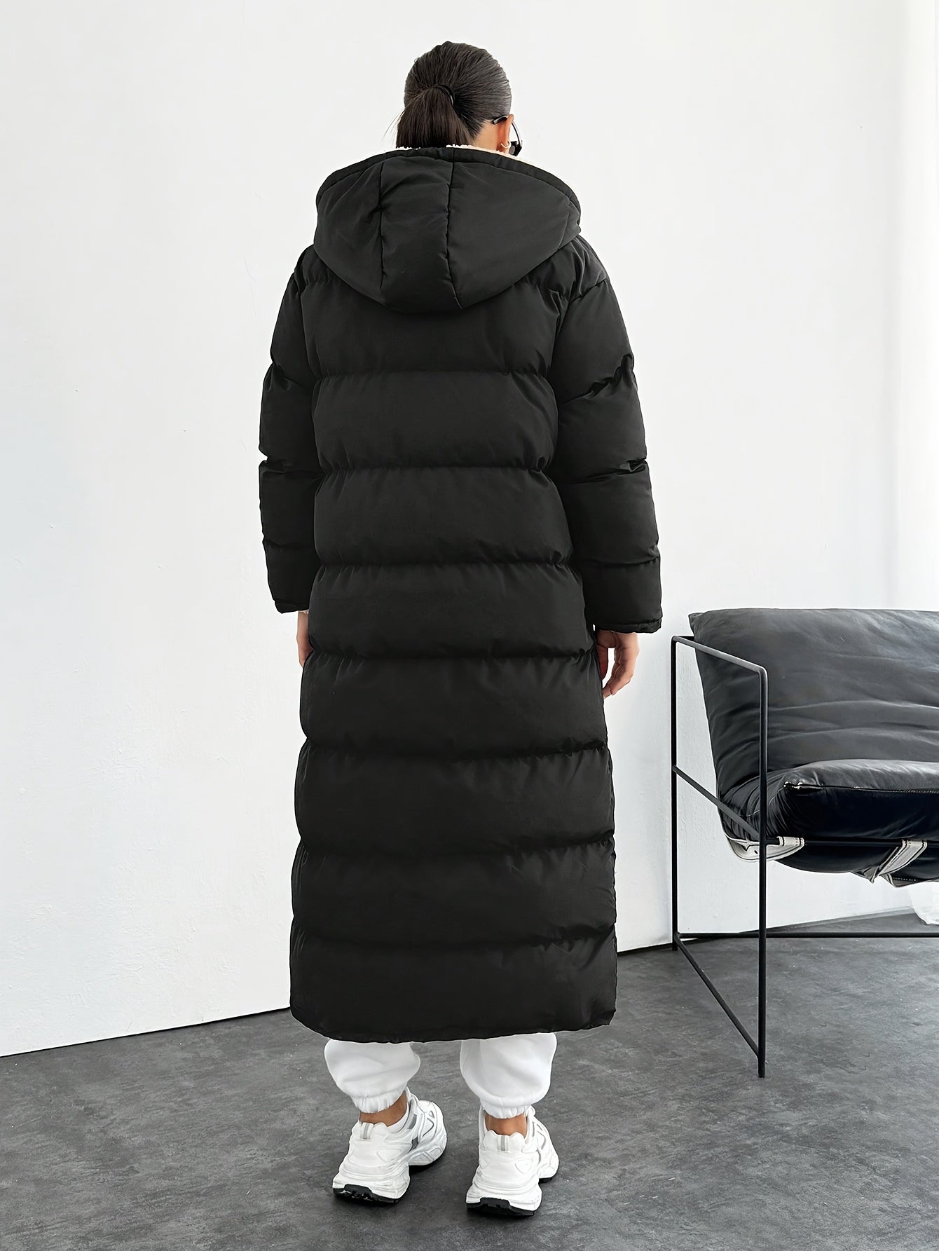 Black elegant long puffer coat for women, windproof with hood and side pockets. Made of machine washable polyester, perfect for cold weather outfits.