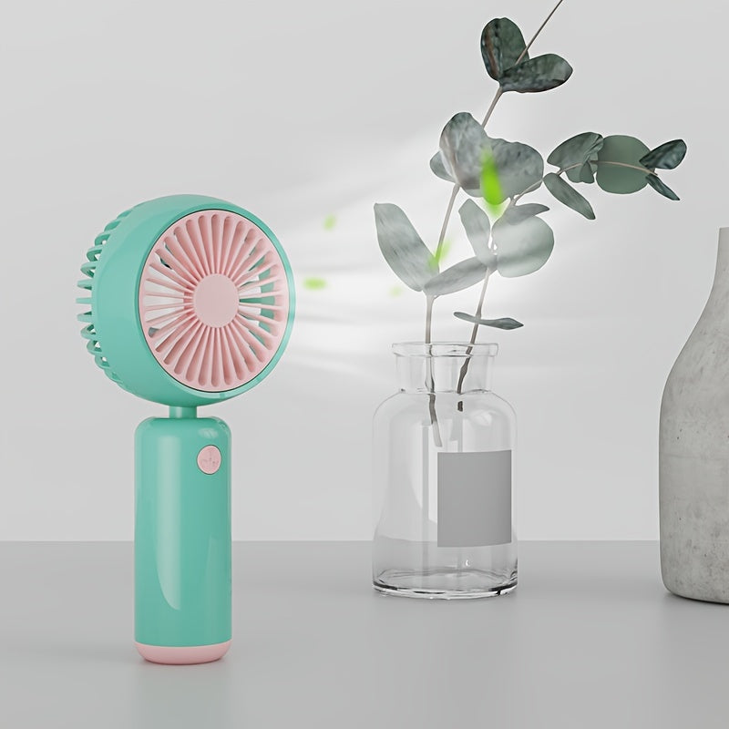 Small handheld portable fan with USB rechargeable battery, three adjustable speeds, and wearable design for use both indoors and outdoors.