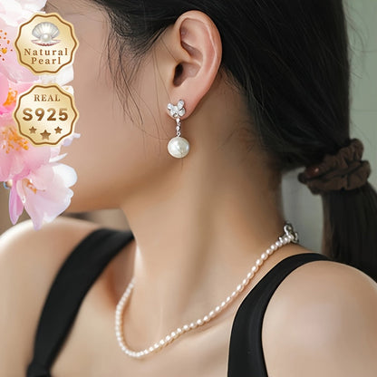 These women's fashionable dangling earrings feature a pair of 12-13mm large grains of strong light, slightly flawed round natural freshwater pearls set in S925 silver. Each earring is adorned with a delicate bow and comes in a gift box. Please note that