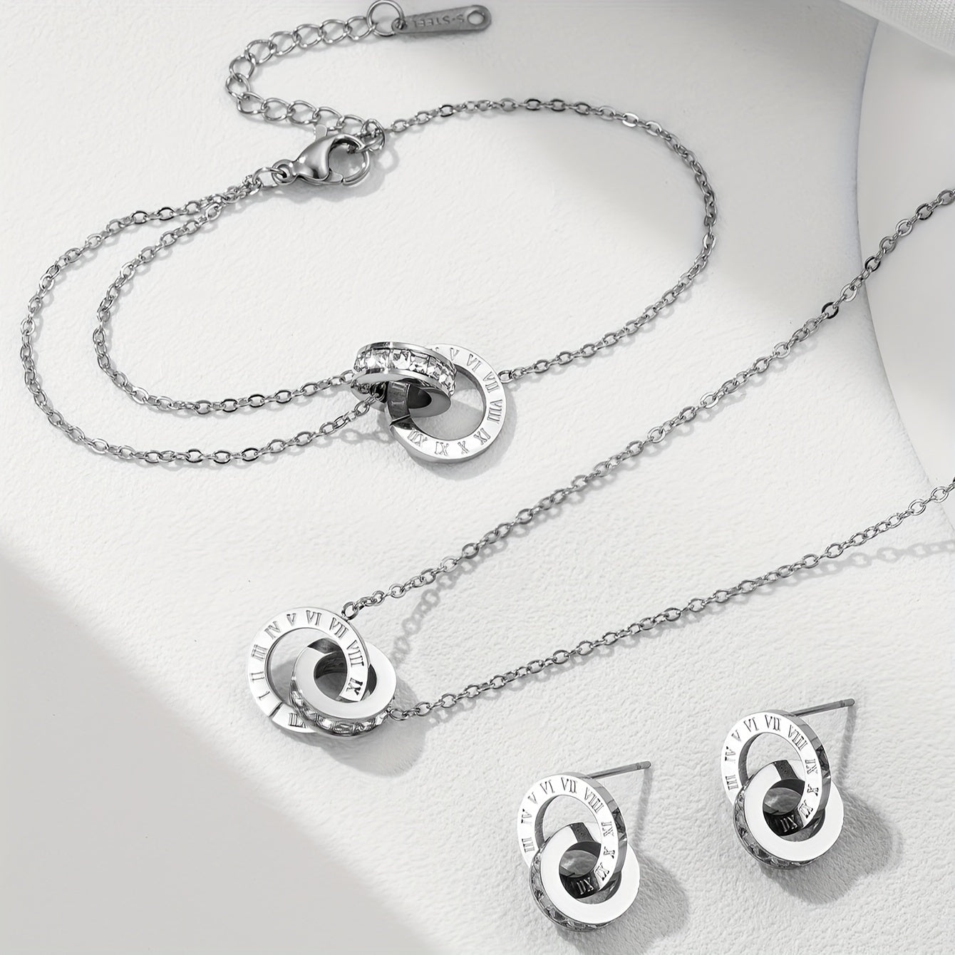 A set of four pieces of stainless steel jewelry featuring silvery precious stones and Roman numerals in a simple, trendy design. This versatile set includes a bracelet, necklace, and earrings, perfect for daily wear or a retro, light luxury holiday